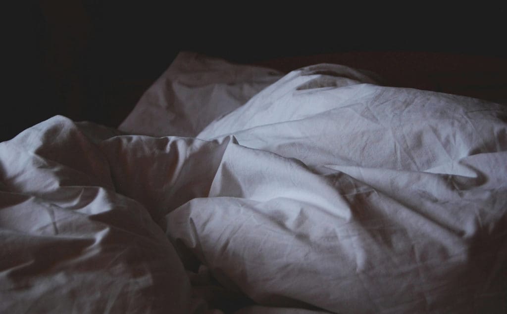 Image of a duvet and pillows on a bed, crinkled surface texture and shadowy light over the image.